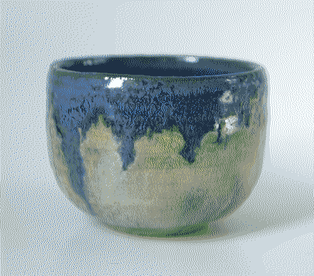 A small wheel-thrown cup. It is cream-colored in the underside, and glazed dark blue in the inside. The blue glaze runs down from the top over the cream color.